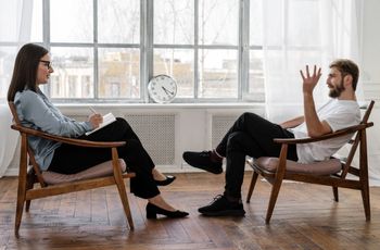 Personnes assises face à face dans des fauteuils, l'une prenant des notes tandis que l'autre s'exprime avec des gestes des mains.