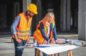 Personnes portant des gilets haute visibilité et un casque de chantier consultant des plans sur une table sur un chantier.