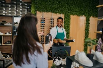 Personne tenant une chaussure devant un espace de vente équipé de présentoirs de chaussures et de lunettes.