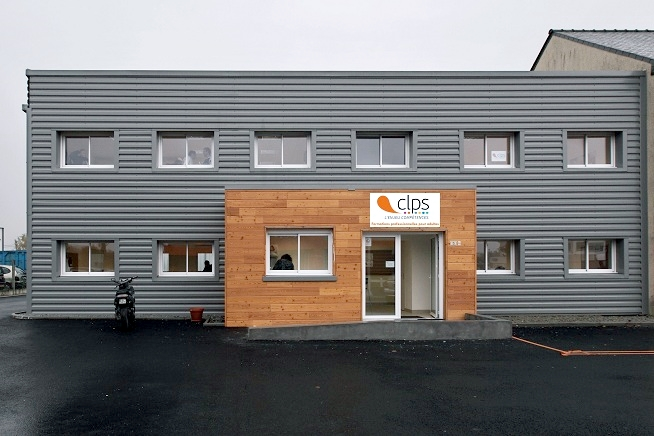 Bâtiment moderne à deux niveaux avec façade en bardage métallique gris et entrée centrale habillée de bois. Le logo du CLPS est affiché au-dessus de la porte d’entrée et plusieurs fenêtres sont réparties sur la façade.