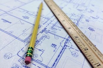 Crayon et règle en bois posés sur un plan technique comportant des schémas, cotes et symboles de dessin.