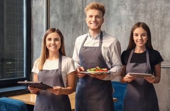 Trois personnes en tenue de service tiennent des plateaux dans une salle de restauration.