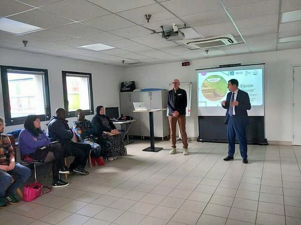 Personnes assises dans une salle de réunion ou de formation assistant à une présentation. Deux intervenants se tiennent devant un écran de projection.