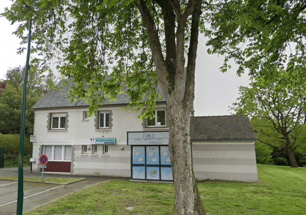 Bâtiment clair à deux niveaux situé dans un espace arboré, avec un grand arbre au premier plan et une entrée portant l'inscription « Pays de Pipriac ».