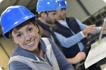 Personnes portant des casques de sécurité bleus dans un environnement industriel. Une femme est au premier plan tandis que deux hommes consultent des documents ou des équipements à l'arrière-plan.