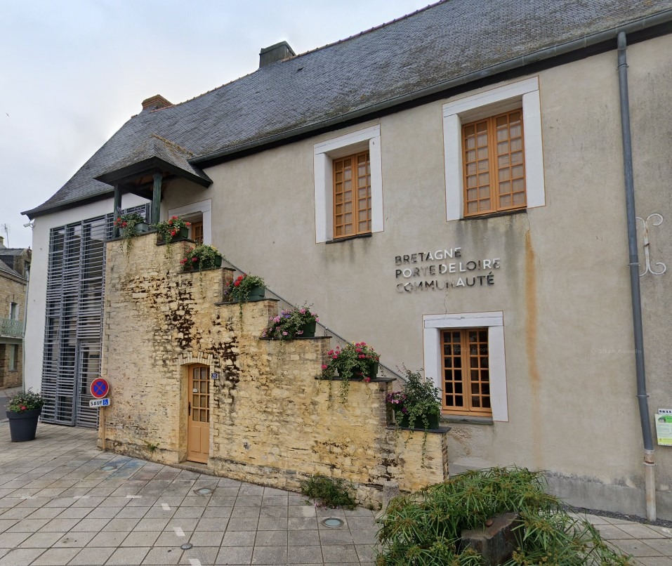 Bâtiment en pierre et enduit clair avec escalier extérieur fleuri, fenêtres à encadrements blancs et inscription « Bretagne Porte de Loire Communauté » sur la façade.