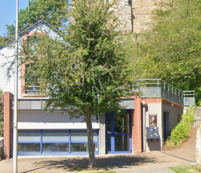 Façade du centre CLPS de Betton avec une entrée vitrée bleue, entourée d’arbres et de végétation.