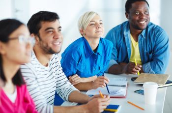 Quatre personnes assises autour d’une table de formation, prenant des notes et travaillant sur des cahiers.