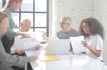 Cinq personnes réunies autour d’une table, consultant des documents et travaillant avec un ordinateur portable.