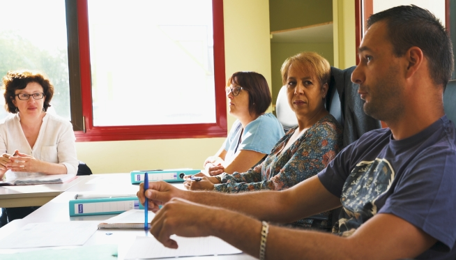 Quatre personnes participent à une réunion autour d’une table avec des documents et des classeurs.