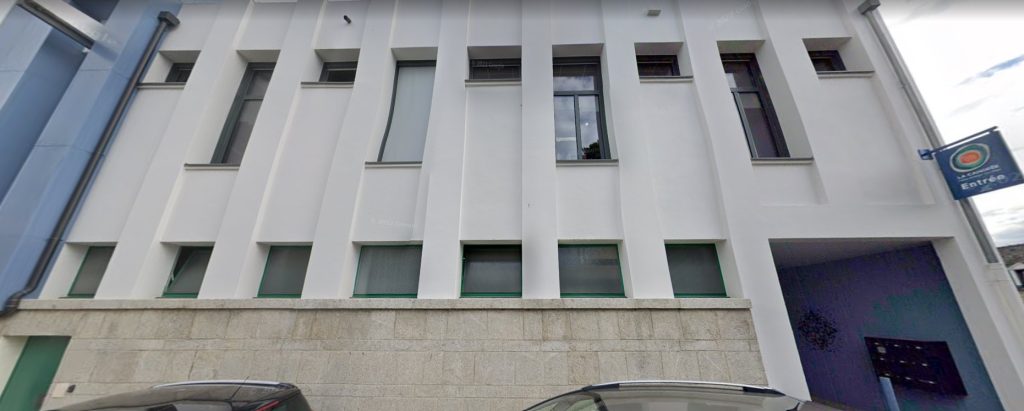 Bâtiment moderne à façade blanche avec hautes fenêtres verticales et entrée couverte.