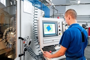 Homme en tenue de travail bleue utilisant un pupitre de commande relié à une machine industrielle automatisée.