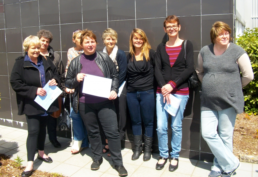 Groupe de huit femmes posant à l'extérieur devant la façade d'un bâtiment. Plusieurs tiennent un document ou un diplôme dans les mains.