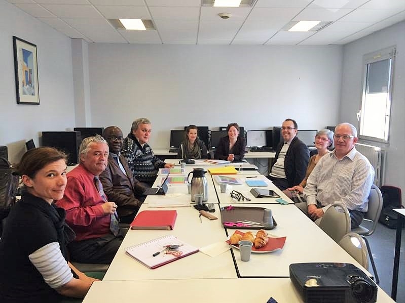 Groupe de personnes assises autour d’une table de réunion dans une salle équipée d’ordinateurs.