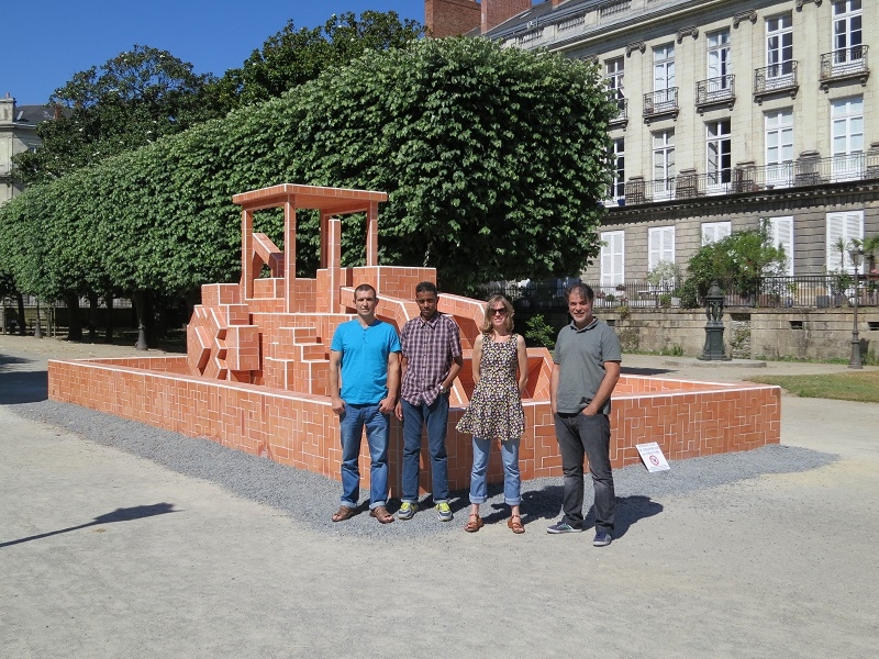 Quatre personnes posent devant une grande sculpture représentant un engin de chantier stylisé.