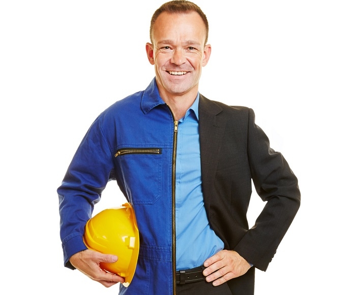 Homme portant une tenue partagée entre une combinaison de travail bleue et une veste de costume noire, tenant un casque de chantier jaune.