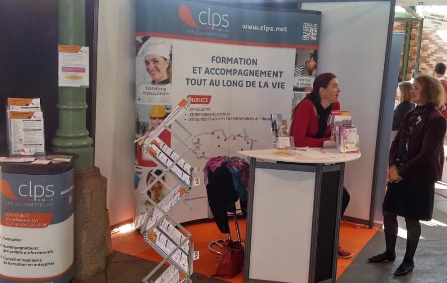 Stand CLPS sur un salon avec une banque d’accueil, des présentoirs de documents et deux personnes échangeant devant un panneau d’information.