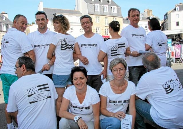 Groupe de onze personnes portant des tee-shirts blancs personnalisés imprimés avec leur mini-CV, réunies sur une place en extérieur.