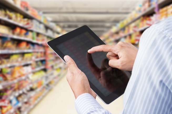 Personne tenant une tablette numérique dans les rayons d'un supermarché ou d'une grande surface.