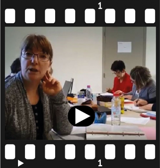Capture d’écran d’une vidéo montrant plusieurs personnes en formation autour de tables dans une salle de cours.