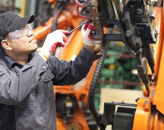 Un homme équipé de lunettes de protection, de gants et d'une tenue de travail réalisant une opération de maintenance sur une machine industrielle.