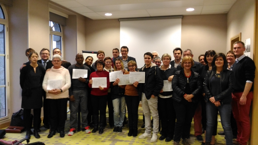 Groupe de personnes réunies dans une salle de réunion. Plusieurs participants tiennent un certificat ou un document devant eux lors d'une photo de groupe.