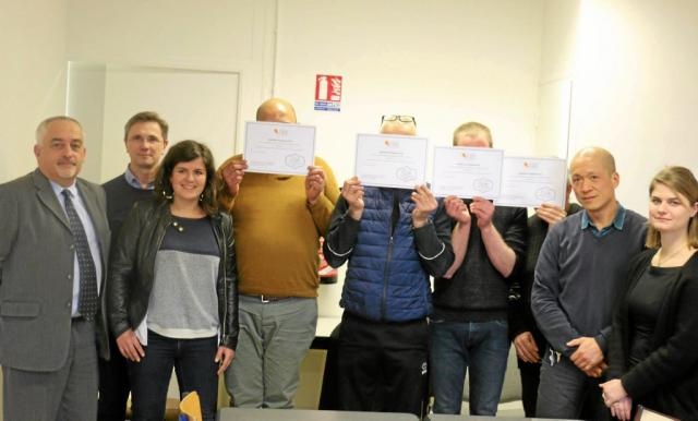 Groupe de personnes réunies dans une salle lors d'une remise de certificats. Quatre détenus présentent un document devant elles tandis que d'autres participants se tiennent à leurs côtés.