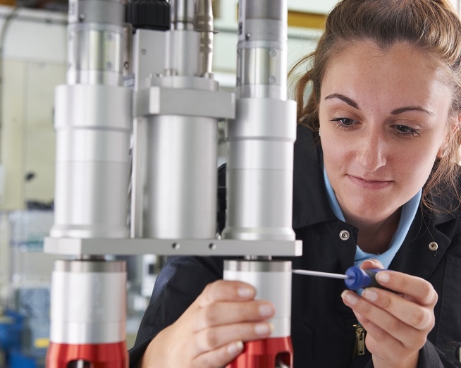 Femme travaillant sur une machine industrielle à l'aide d'un tournevis dans un atelier de production.