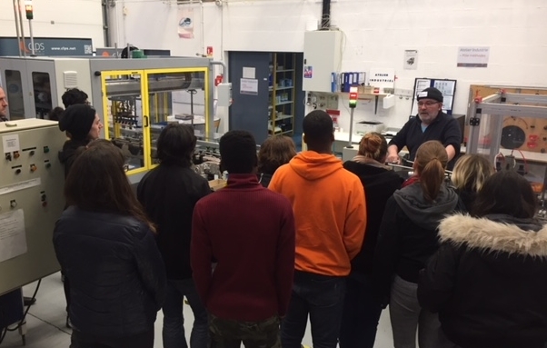 Groupe de personnes rassemblées dans un atelier industriel autour d'un équipement de production automatisé. Un homme présente le fonctionnement de la machine au groupe.