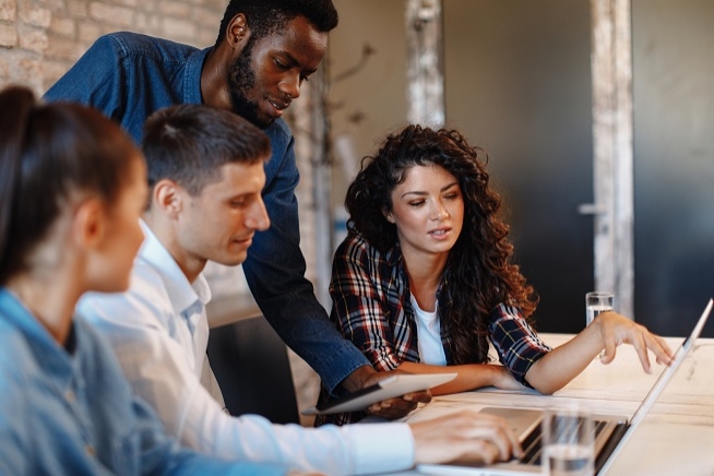 Groupe de quatre personnes réunies autour d’une table, travaillant ensemble sur un ordinateur portable et des documents.