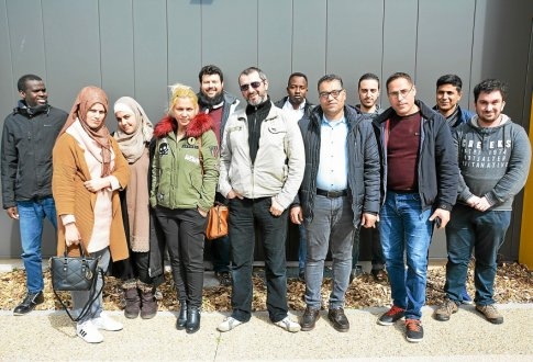 Groupe de douze personnes posant côte à côte devant la façade d’un bâtiment moderne.