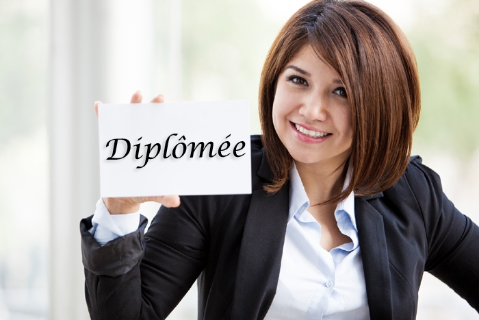 Femme tenant un feuille sur lequel est écrit « Diplômée » devant un fond clair.