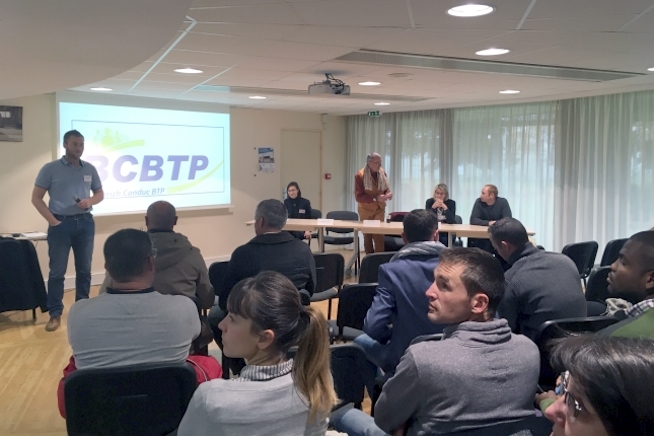 Participants assis dans une salle de réunion faisant face à une table d'intervenants. Un écran de projection affiche le logo « BCBTP » au devant de la salle.