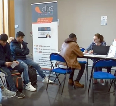 Plusieurs personnes sont assises dans un espace d'accueil ou de recrutement. Deux personnes échangent autour d'une table équipée d'un ordinateur portable tandis que d'autres attendent à proximité.