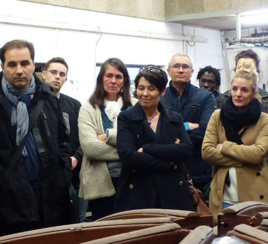 Groupe de personnes réunies dans un atelier autour d'une structure métallique de grande dimension en cours de fabrication.