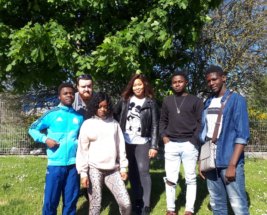 Groupe de six jeunes posant à l'extérieur sur une pelouse devant des arbres. Les personnes sont réunies côte à côte dans un espace vert.