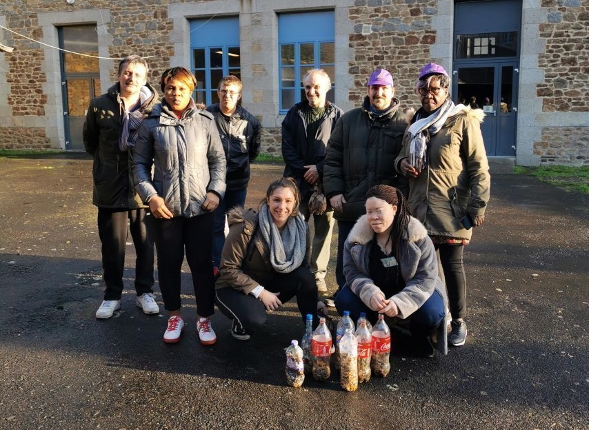 Groupe de stagiaires réuni à l'extérieur devant un bâtiment. Plusieurs bouteilles remplies de mégots de cigarettes sont disposées au sol devant le groupe.