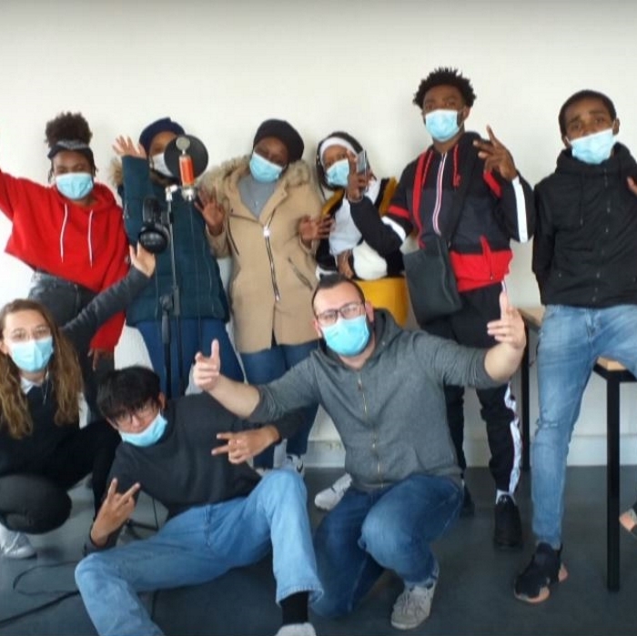 Groupe de neuf personnes portant des masques chirurgicaux dans une salle équipée de matériel d'enregistrement audio. Un microphone avec filtre anti-pop est installé au premier plan tandis que plusieurs personnes prennent la pose face à l'appareil photo.