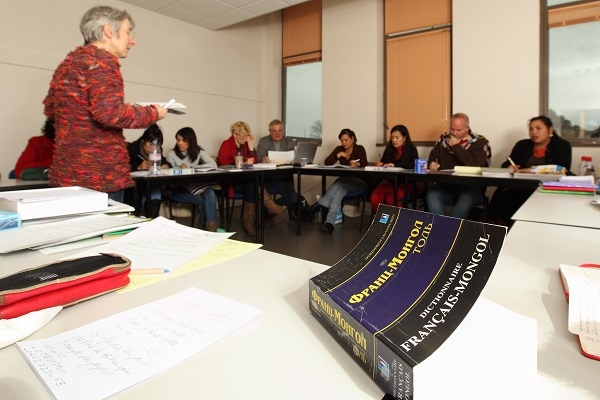 Salle de formation avec plusieurs personnes assises autour de tables disposées en U. Un dictionnaire français est visible au premier plan.