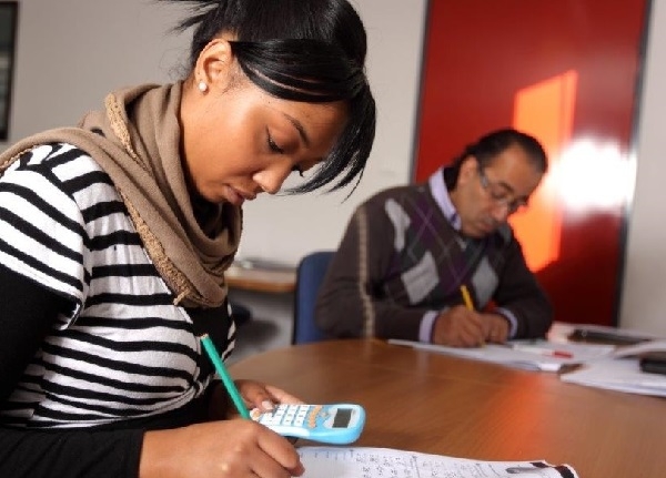 Deux personnes sont assises à une table de formation. L'une utilise une calculatrice et écrit sur une feuille pendant qu'une autre complète également des documents.